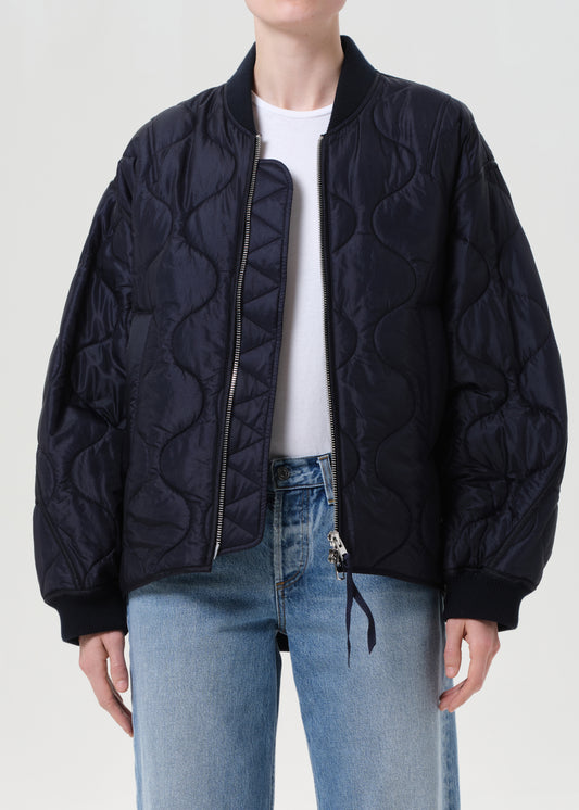 Person wearing a navy quilted jacket and light blue jeans on a white background