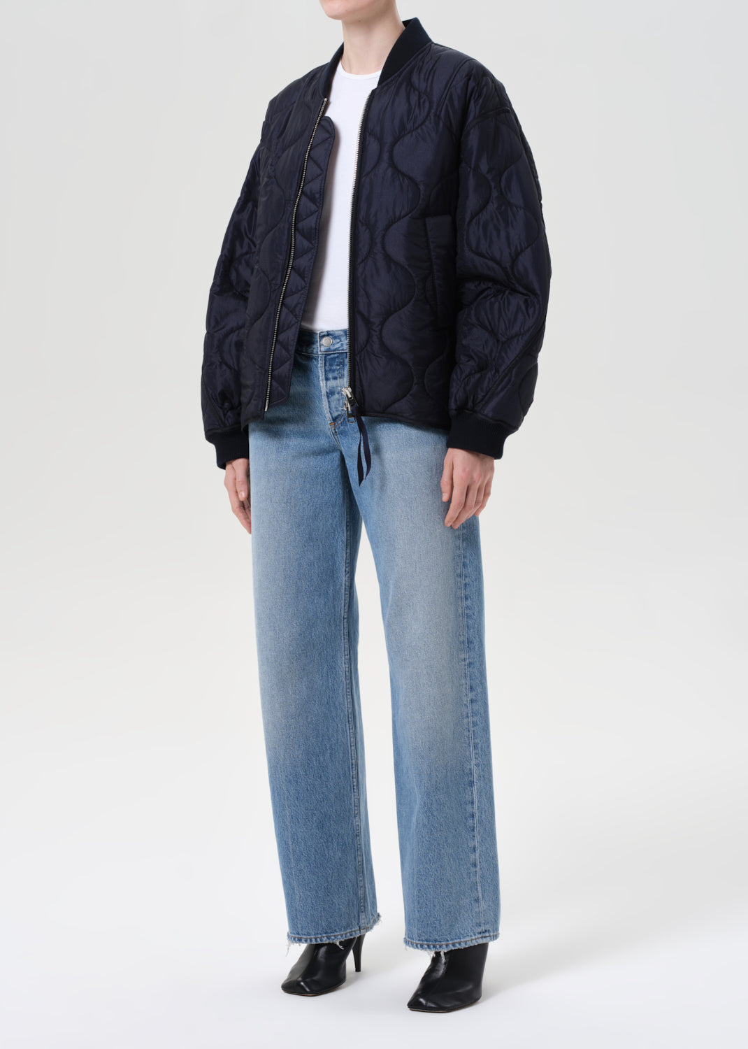 Person wearing a black quilted jacket and blue jeans on a white background