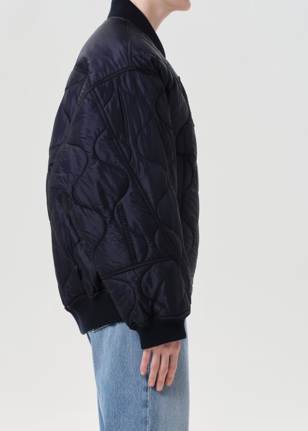 Person wearing a dark quilted jacket and light blue jeans on a white background