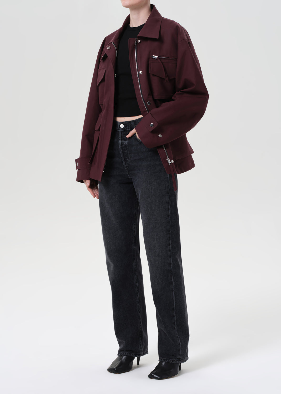 Person wearing a burgundy jacket and black jeans on a white background