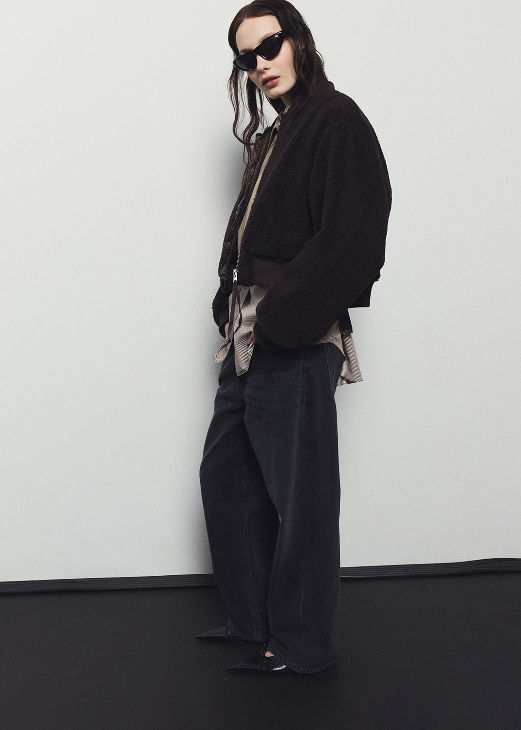 Person wearing a black outfit with sunglasses against a white wall