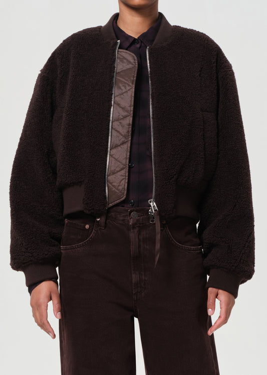Person wearing a dark brown jacket with a textured pattern on a plain background