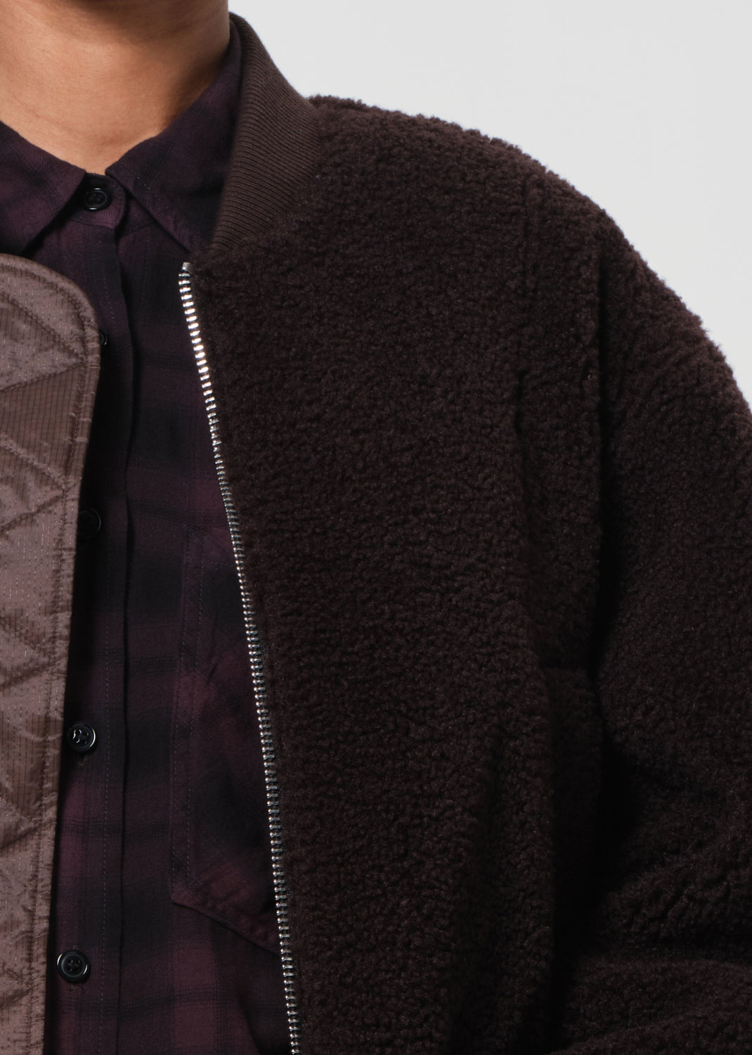 Close-up of a dark brown textured jacket with a zipper on a neutral background