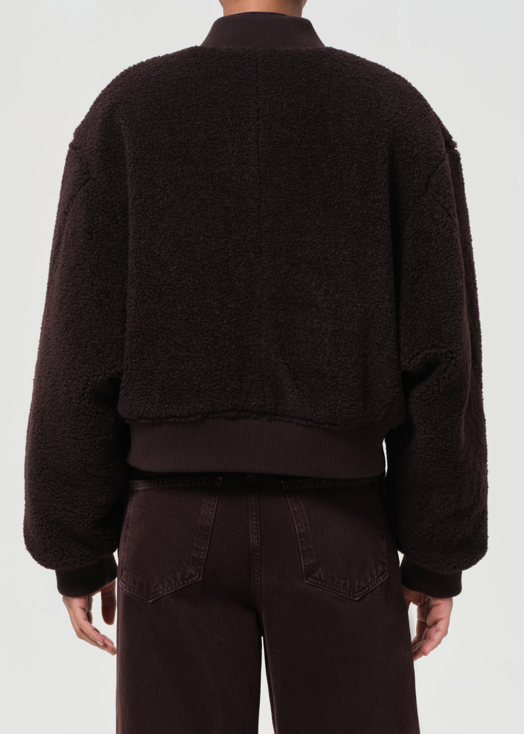 Person wearing a dark brown fleece jacket and pants on a white background