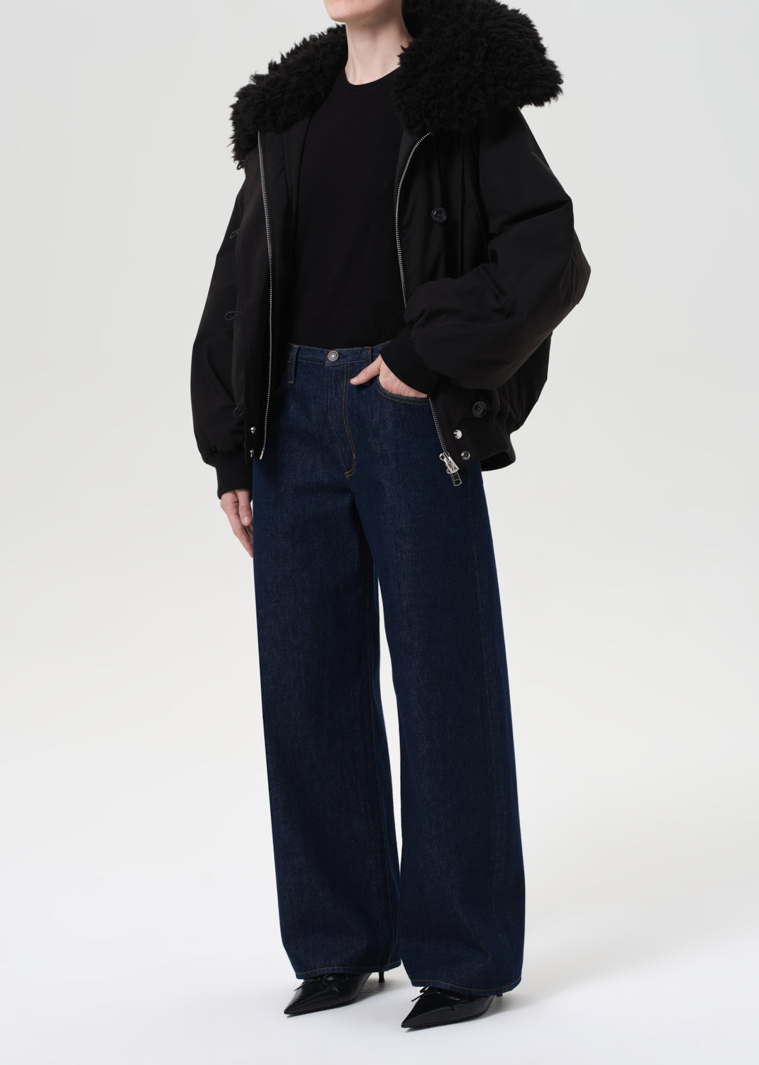 Person wearing a black jacket with fur collar and dark jeans on a white background