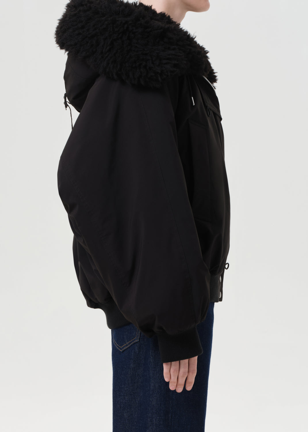 Person wearing a black jacket with a fur-lined hood on a plain background