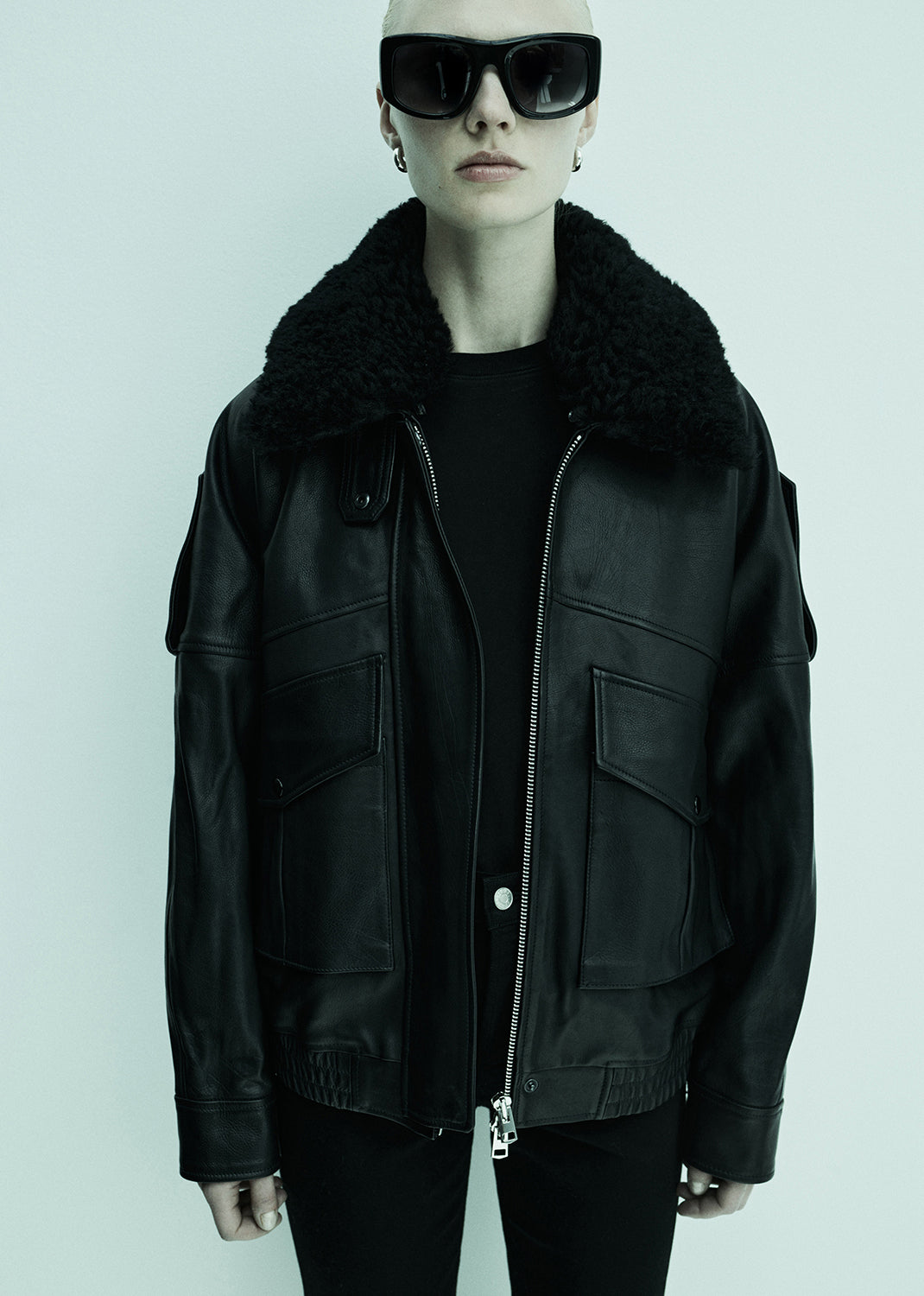 Person wearing a black leather jacket with fur collar on a light gray background