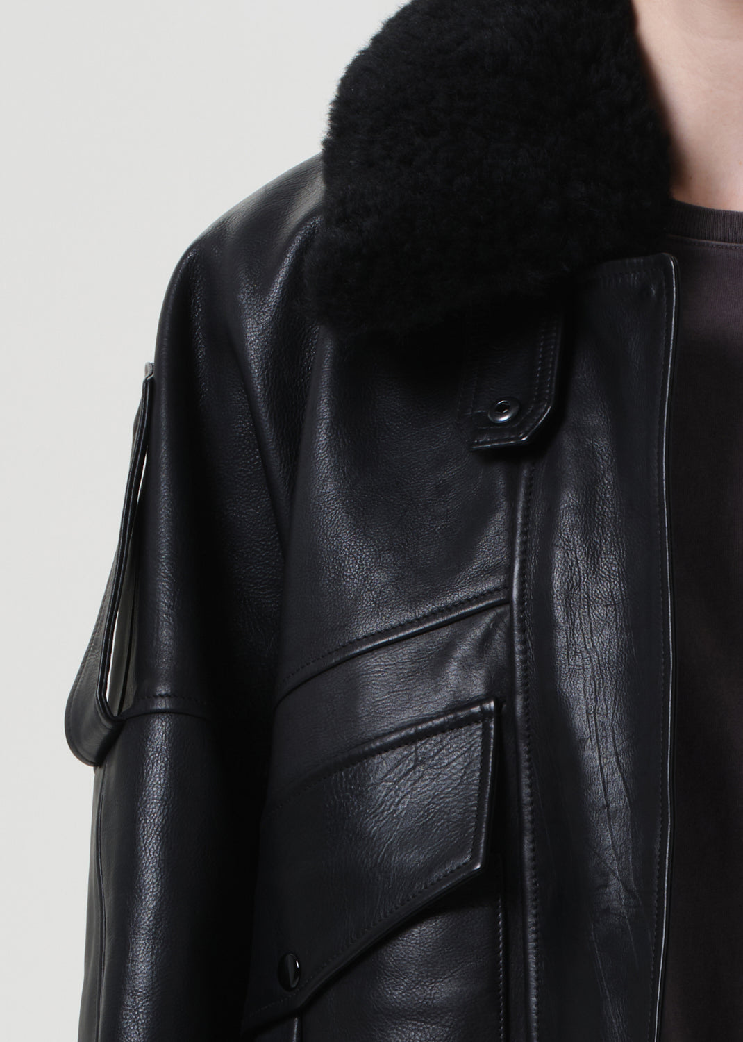 Close-up of a black leather jacket with fur collar on a light gray background
