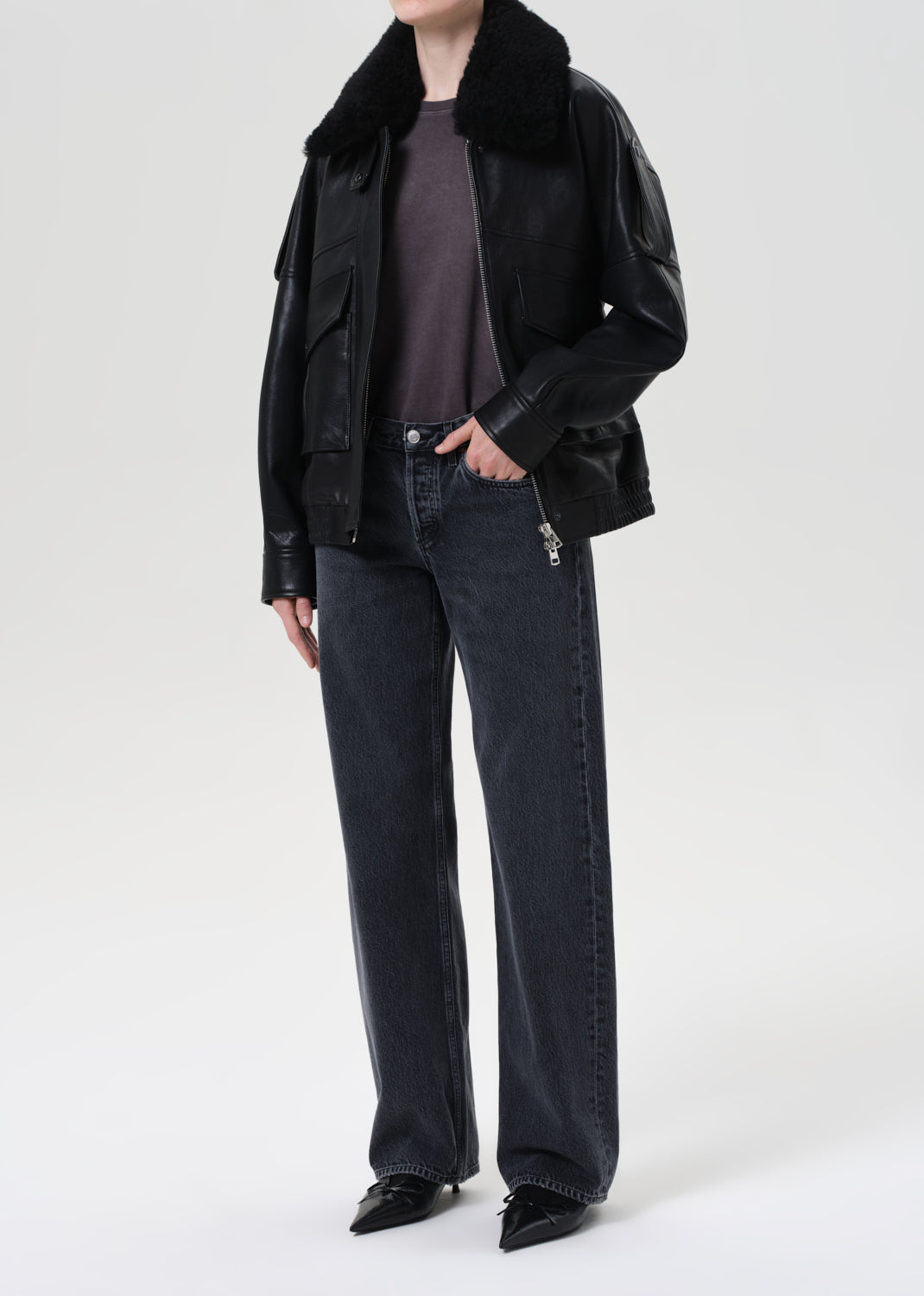 Person wearing a black jacket with fur collar and dark jeans on a white background