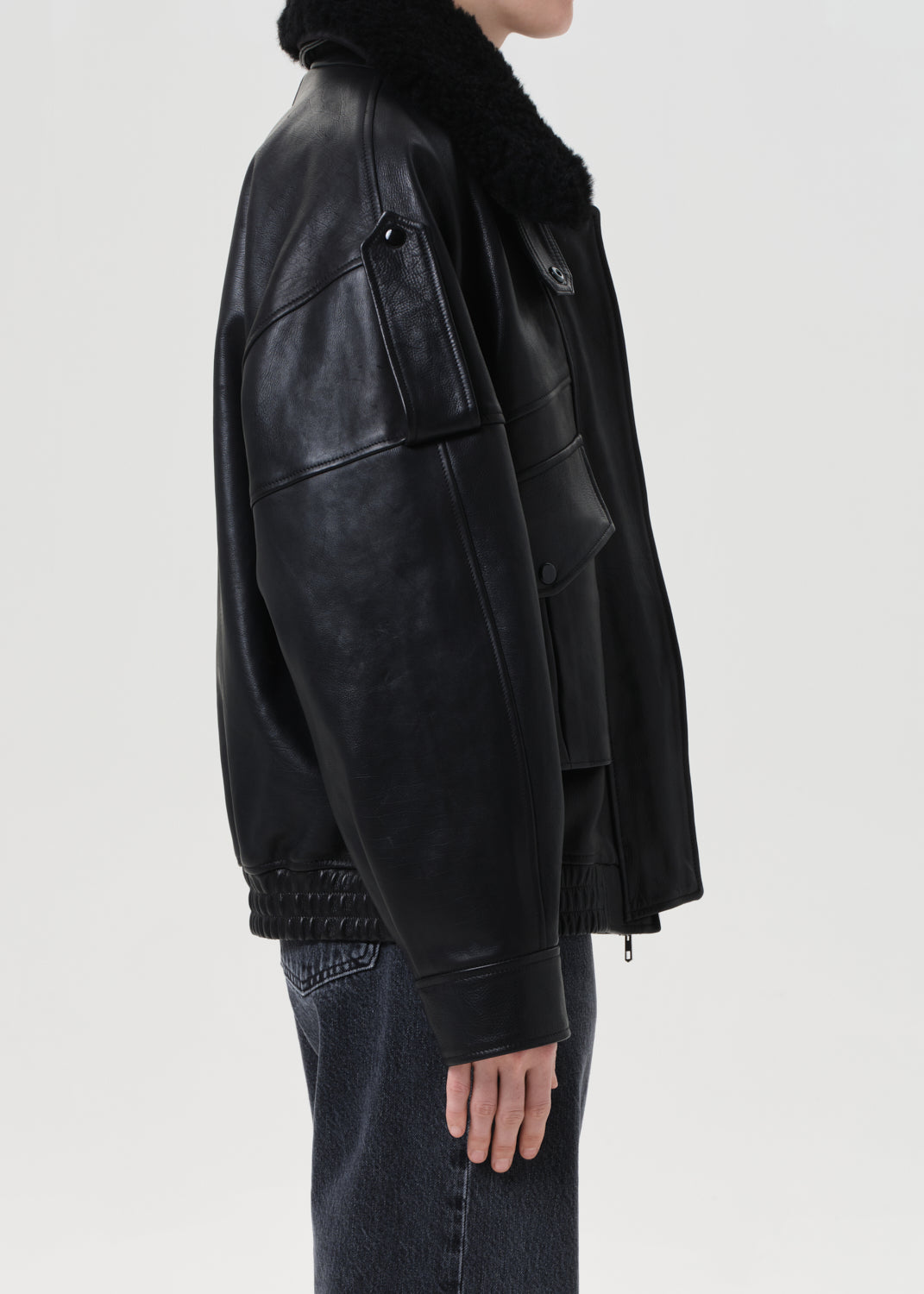 Black leather jacket with fur collar worn by a person on a light gray background