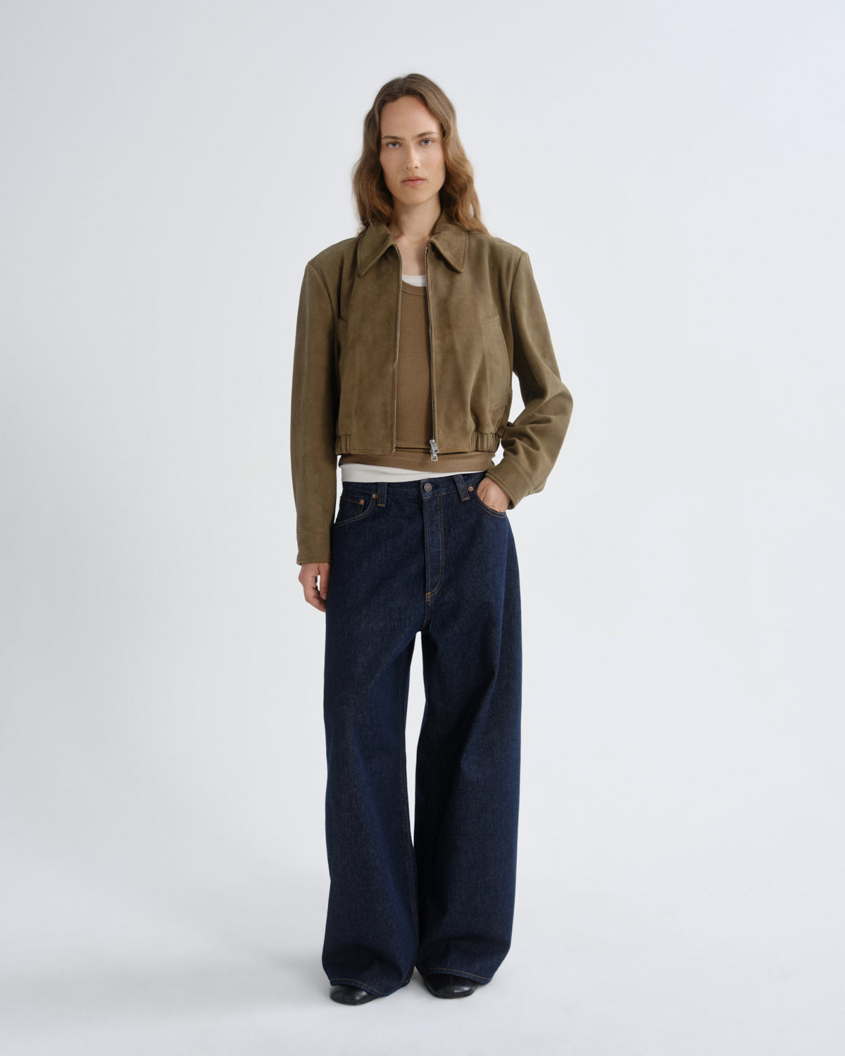 Person wearing a brown jacket and dark blue jeans on a white background