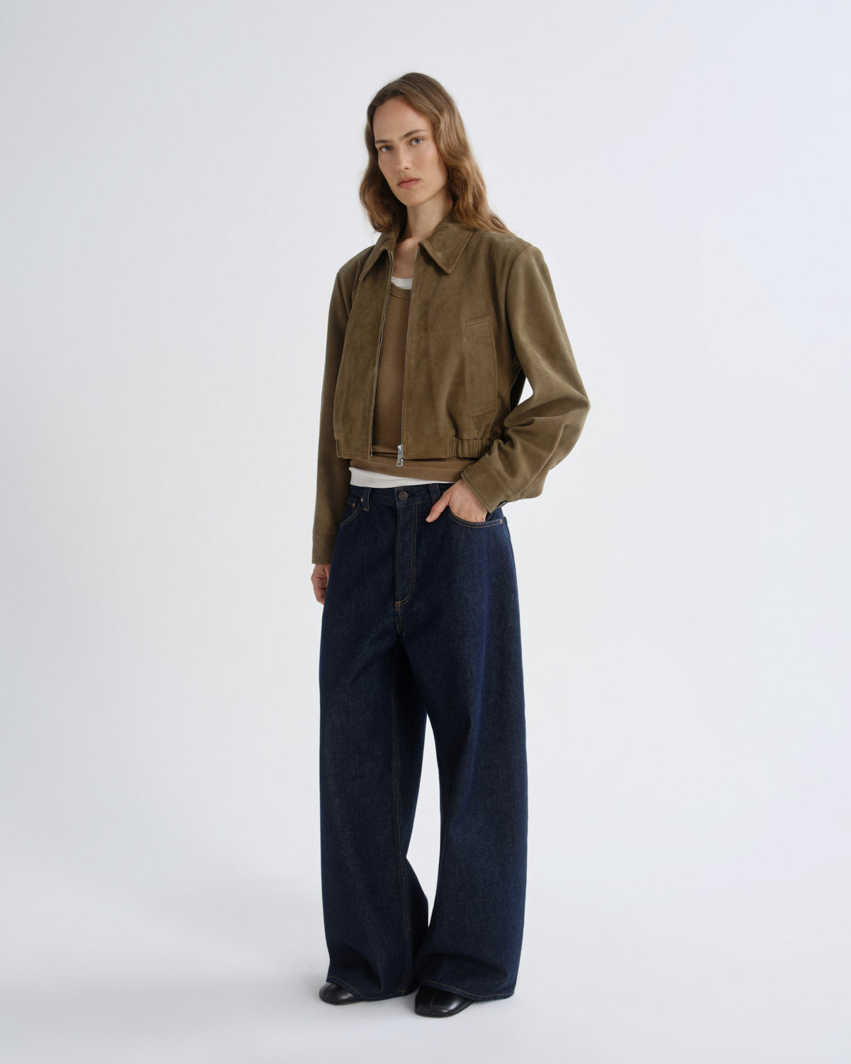 Woman wearing a brown jacket and dark blue jeans on a white background