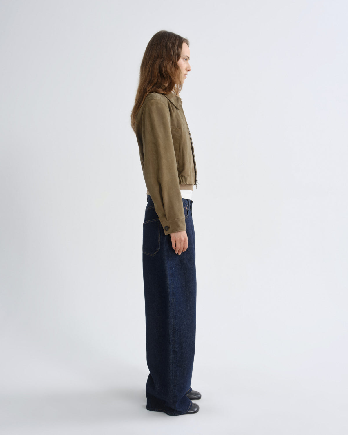Person wearing a green jacket and dark blue jeans on a white background