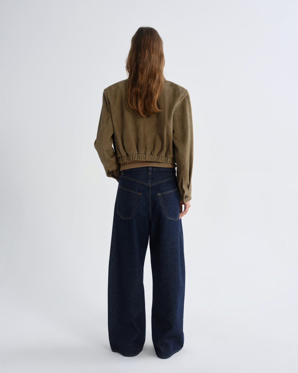 Person wearing a green jacket and dark blue jeans on a white background