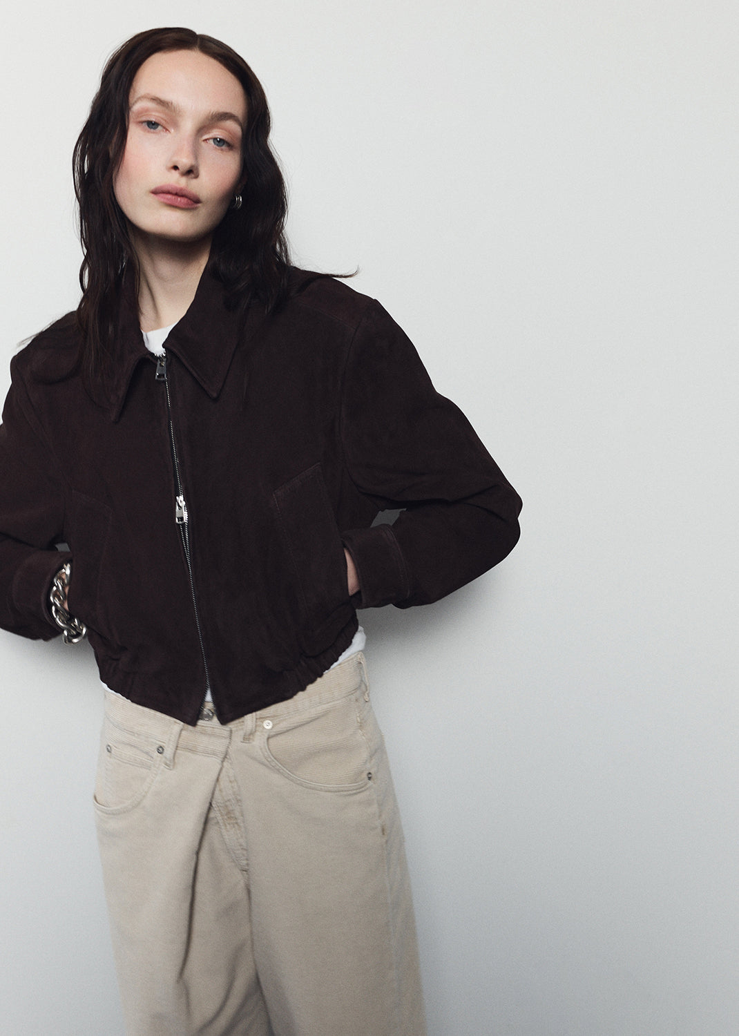 Person wearing a black jacket and beige pants against a white background