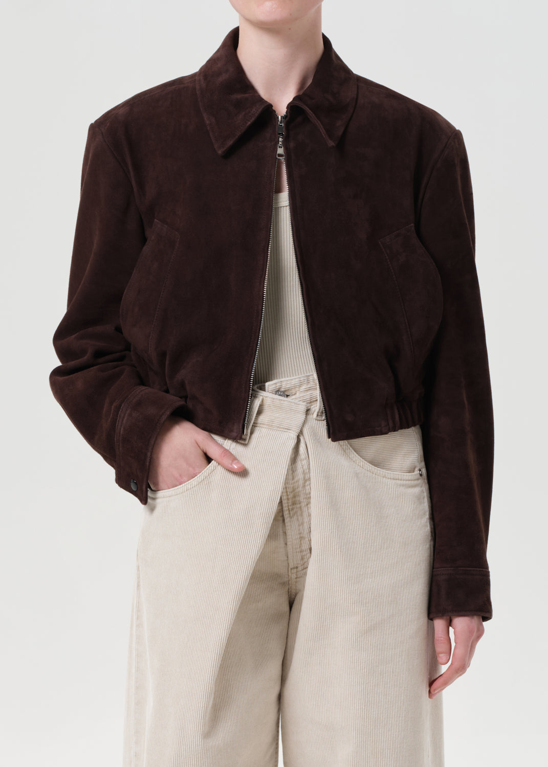 Person wearing a brown jacket and beige pants on a white background