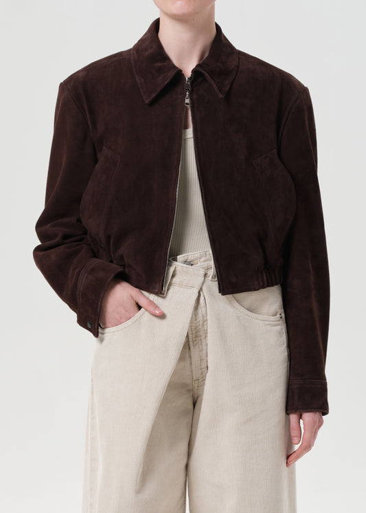 Person wearing a brown jacket and beige pants on a white background