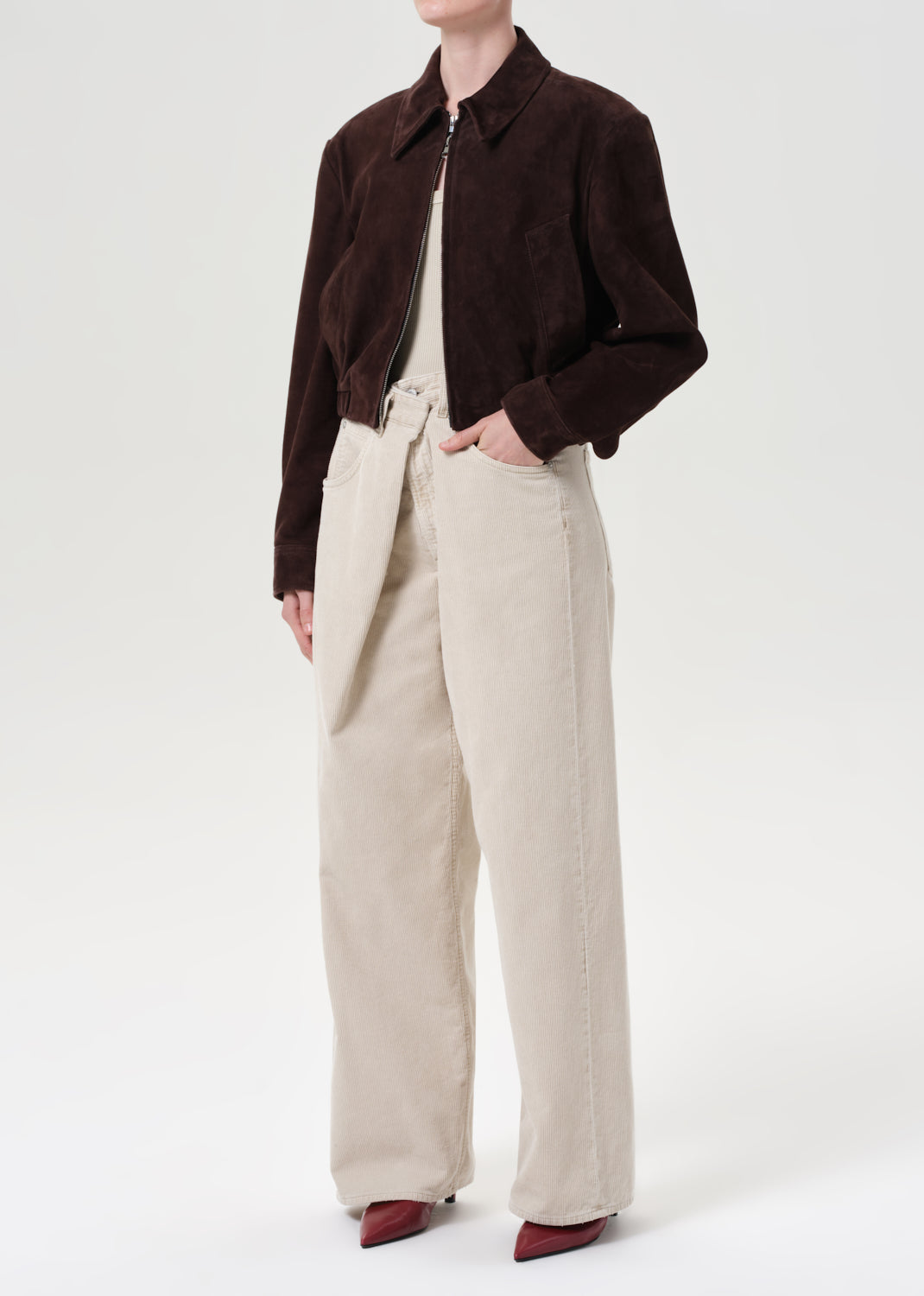 Person wearing a brown jacket and beige pants on a white background