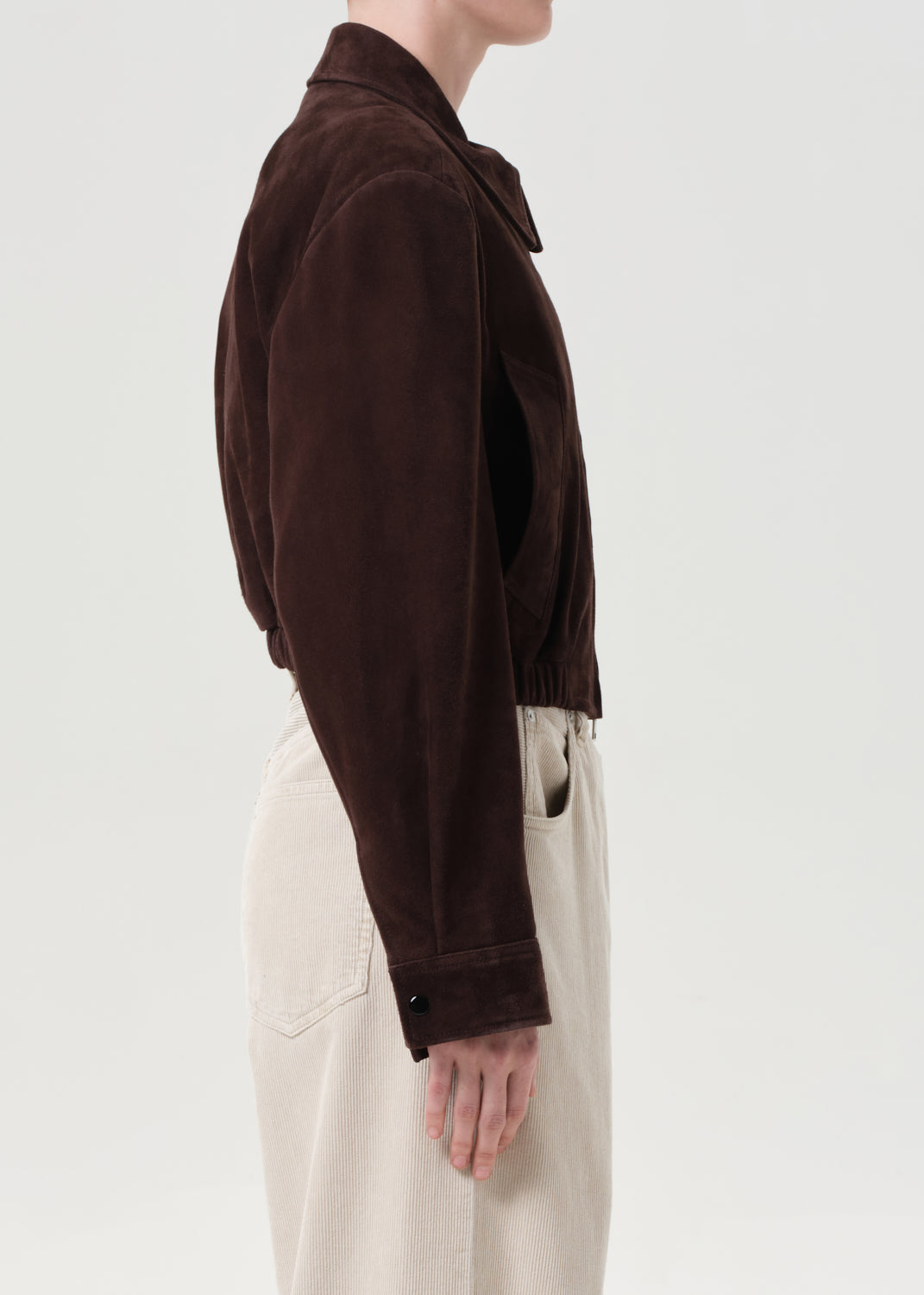 Person wearing a brown jacket and beige pants on a light gray background