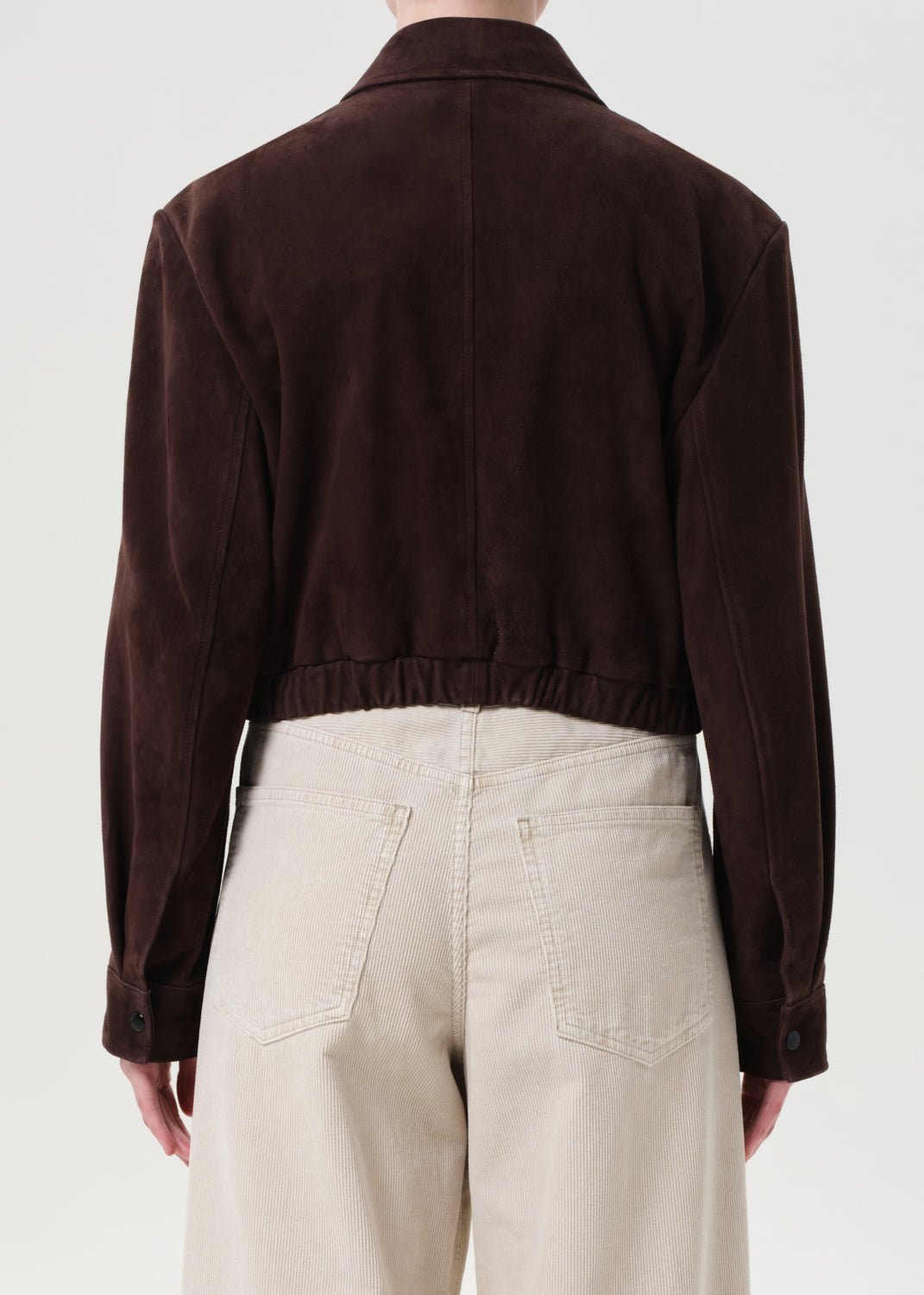 Person wearing a brown jacket and beige pants on a white background