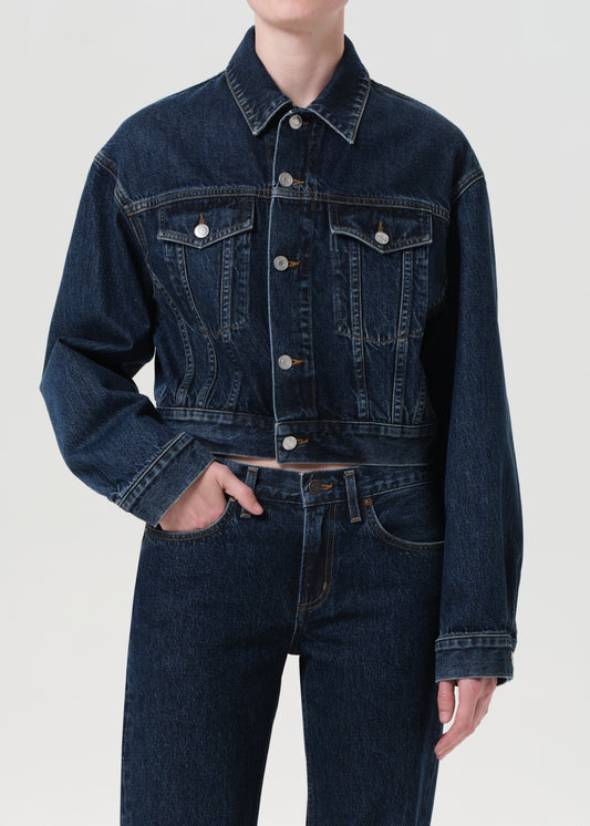 Person wearing a dark blue denim jacket and jeans on a light gray background