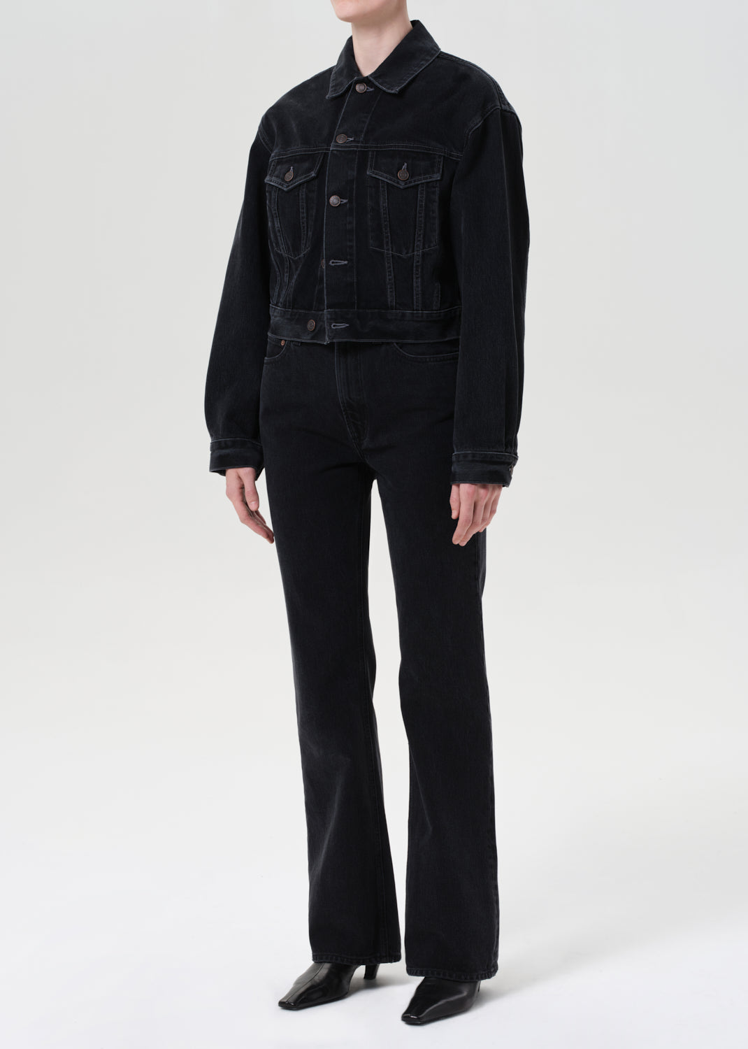 Person wearing a black denim jacket and black pants on a white background