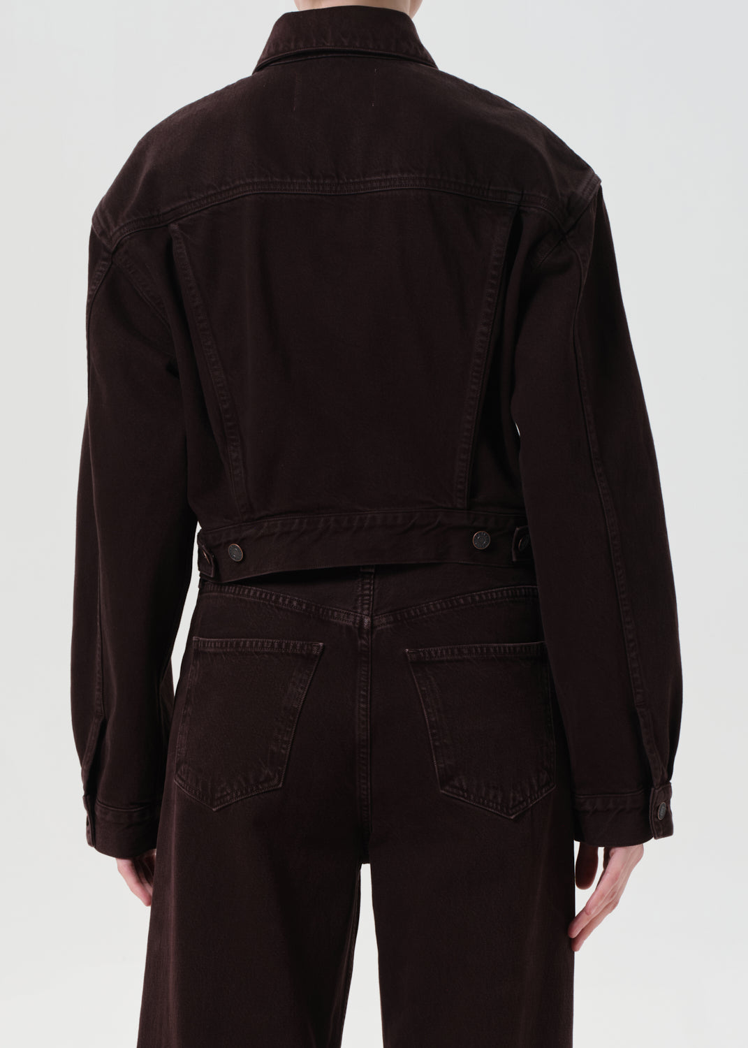 Person wearing a dark brown jacket and pants on a white background