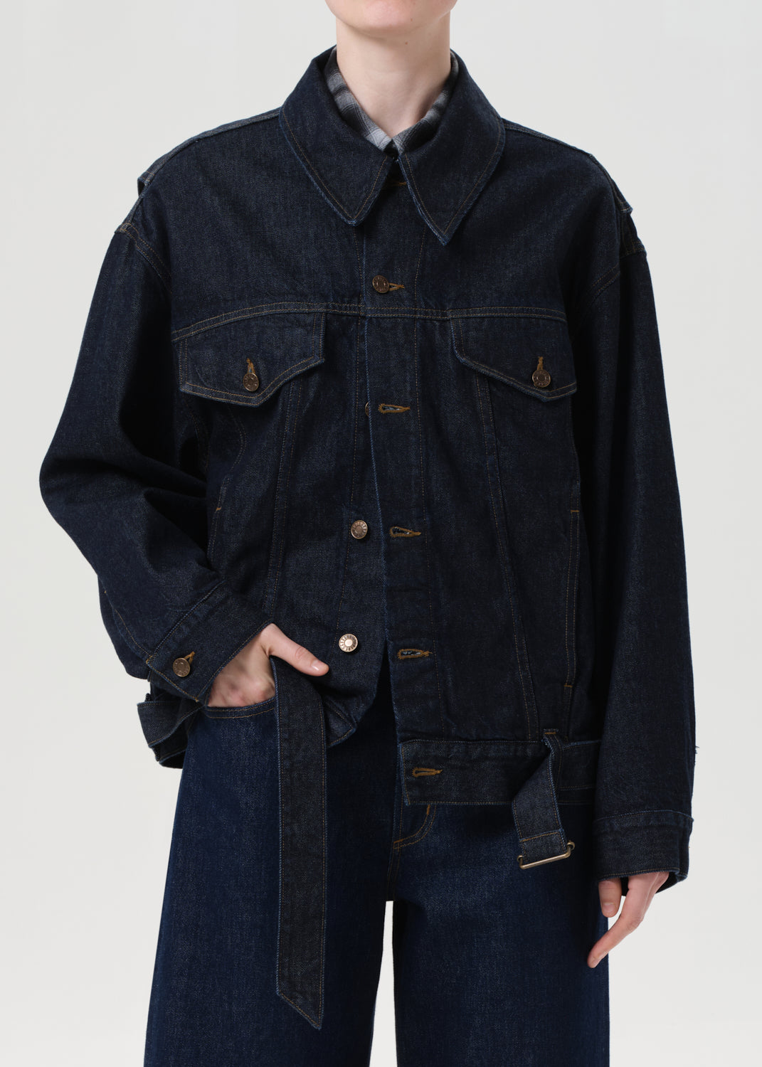 Person wearing a dark denim jacket and jeans on a plain background