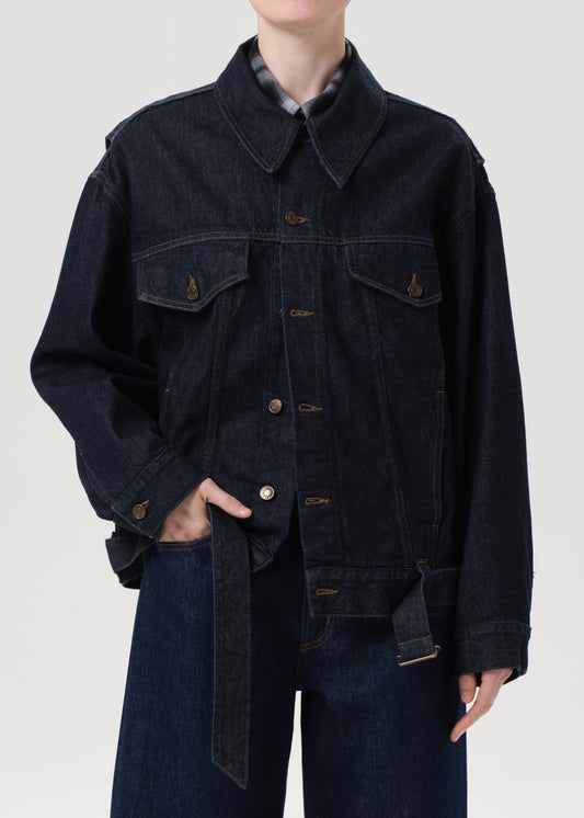 Person wearing a dark denim jacket and jeans on a plain background