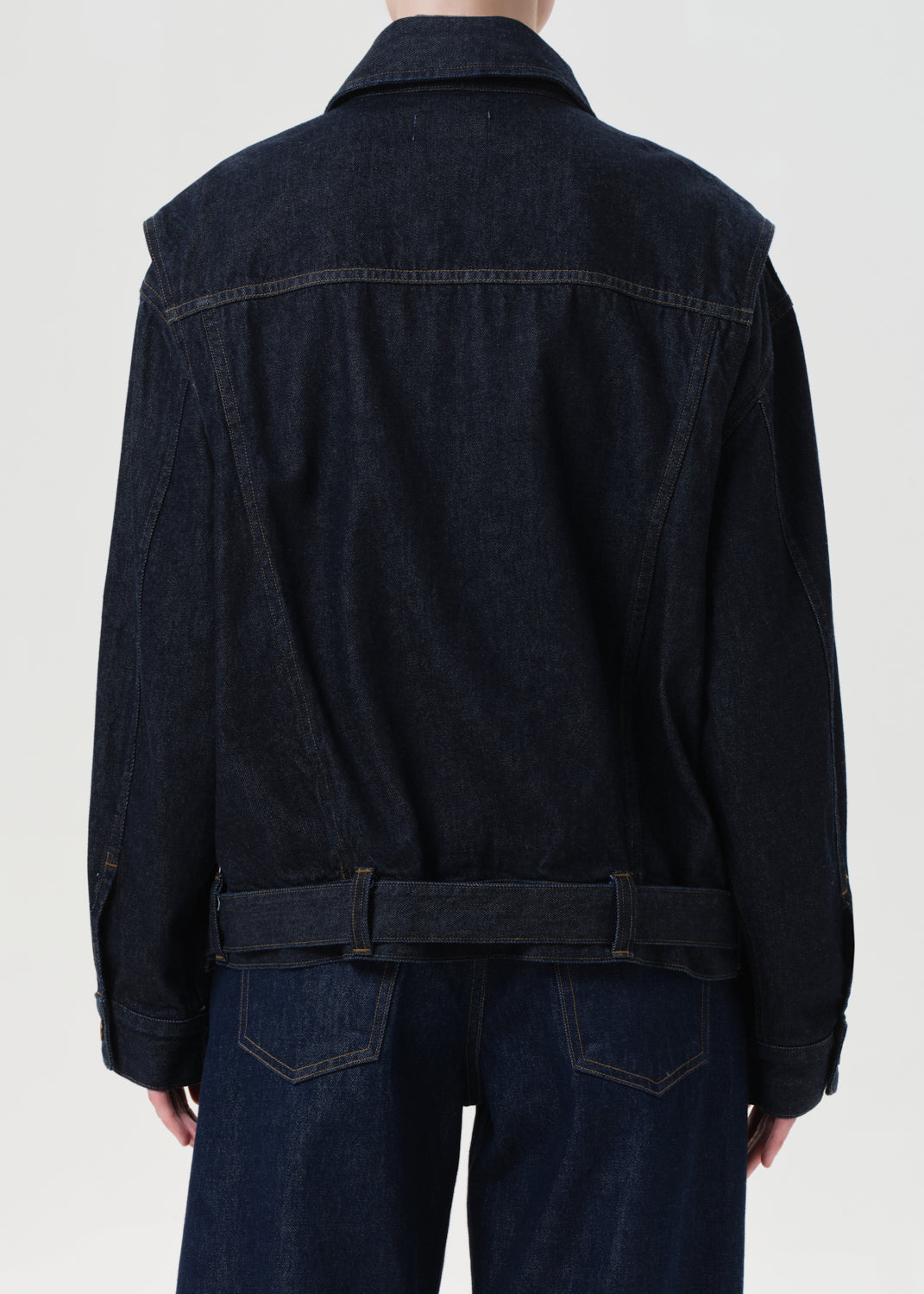 Person wearing a dark denim jacket and jeans on a white background