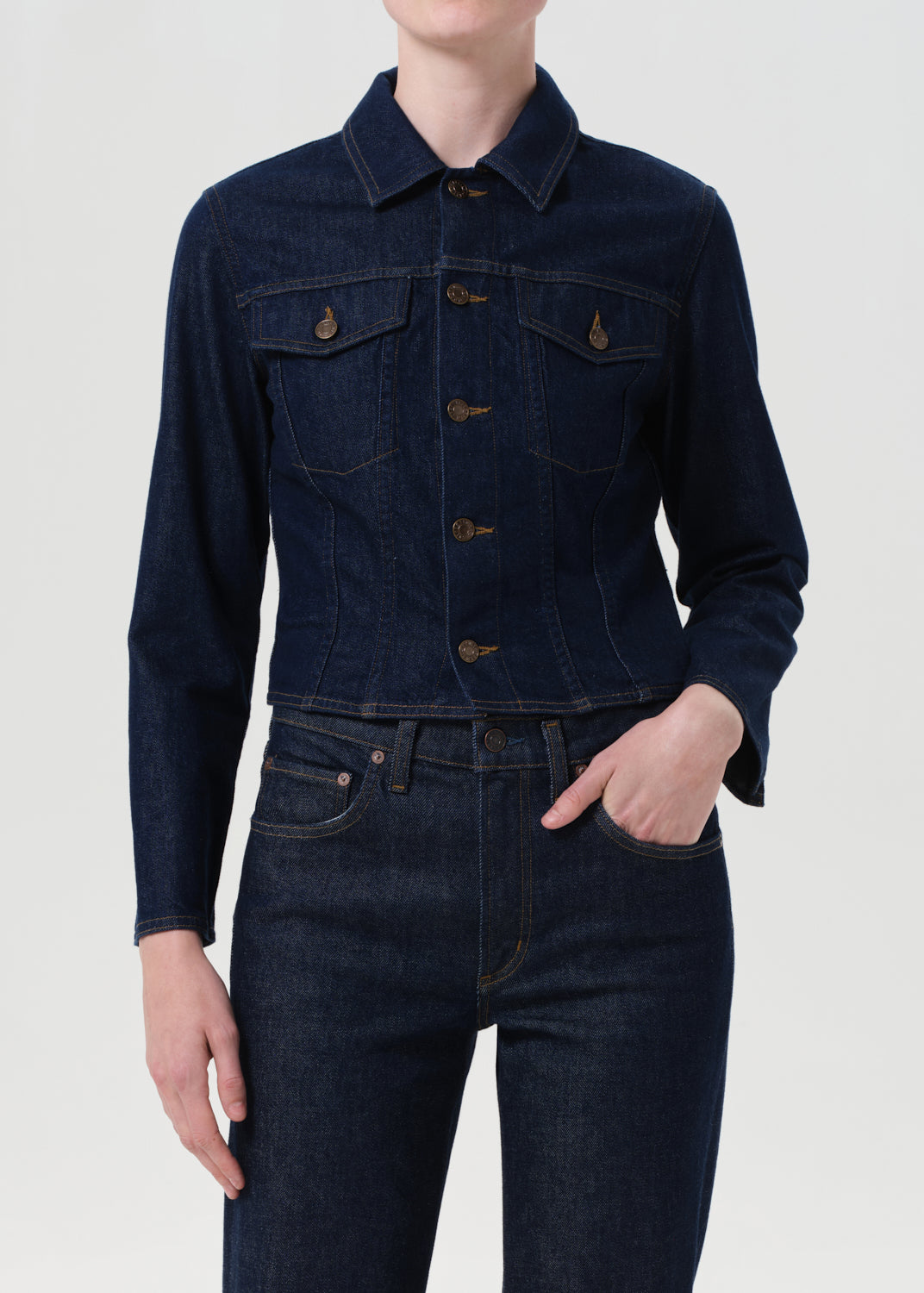 Person wearing a dark denim jacket and jeans on a white background