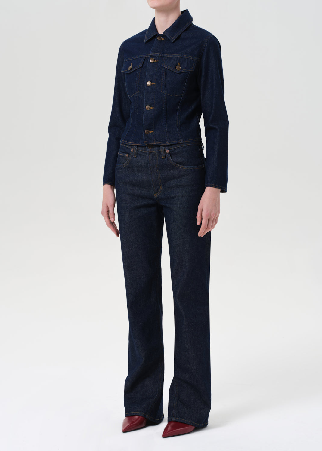 Person wearing a dark denim jacket and jeans on a white background