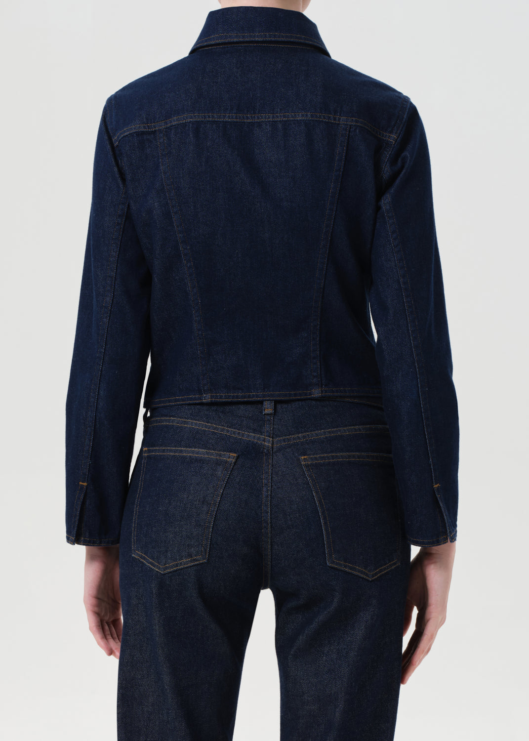 Person wearing a dark blue denim jacket and pants on a white background
