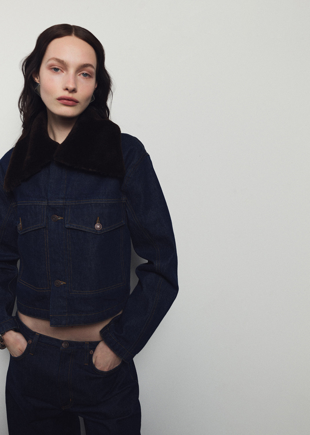 Person wearing a dark denim jacket and pants against a plain background