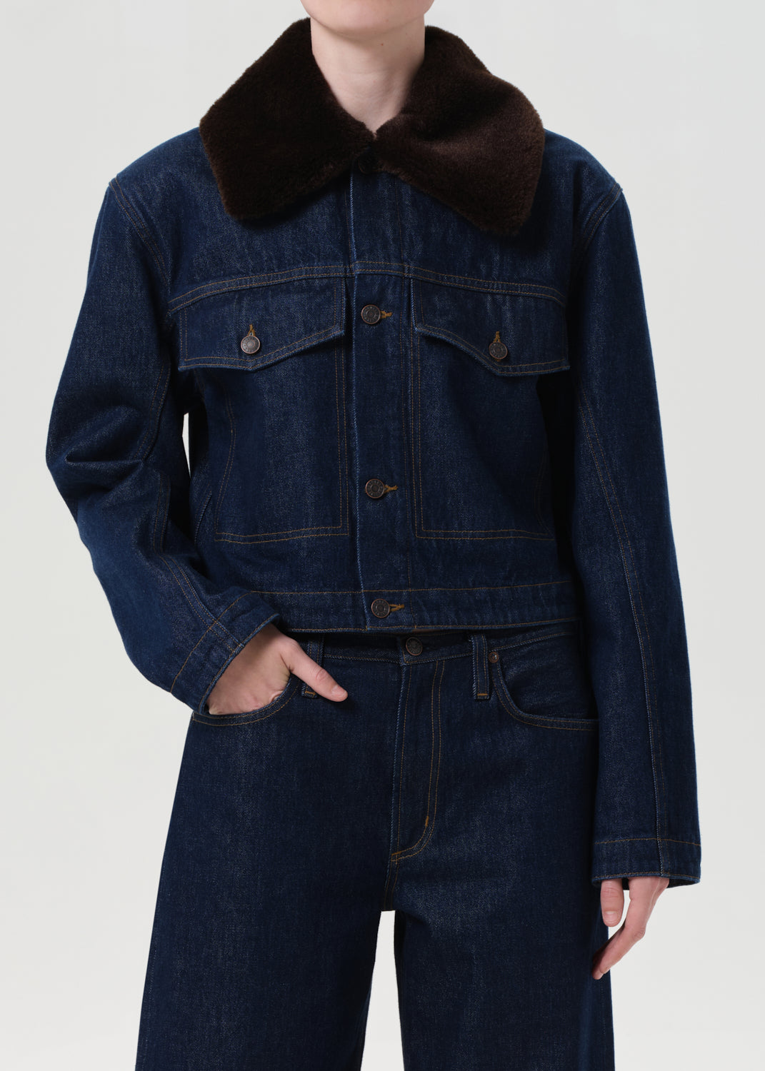 Person wearing a dark blue denim jacket with a brown fur collar on a white background