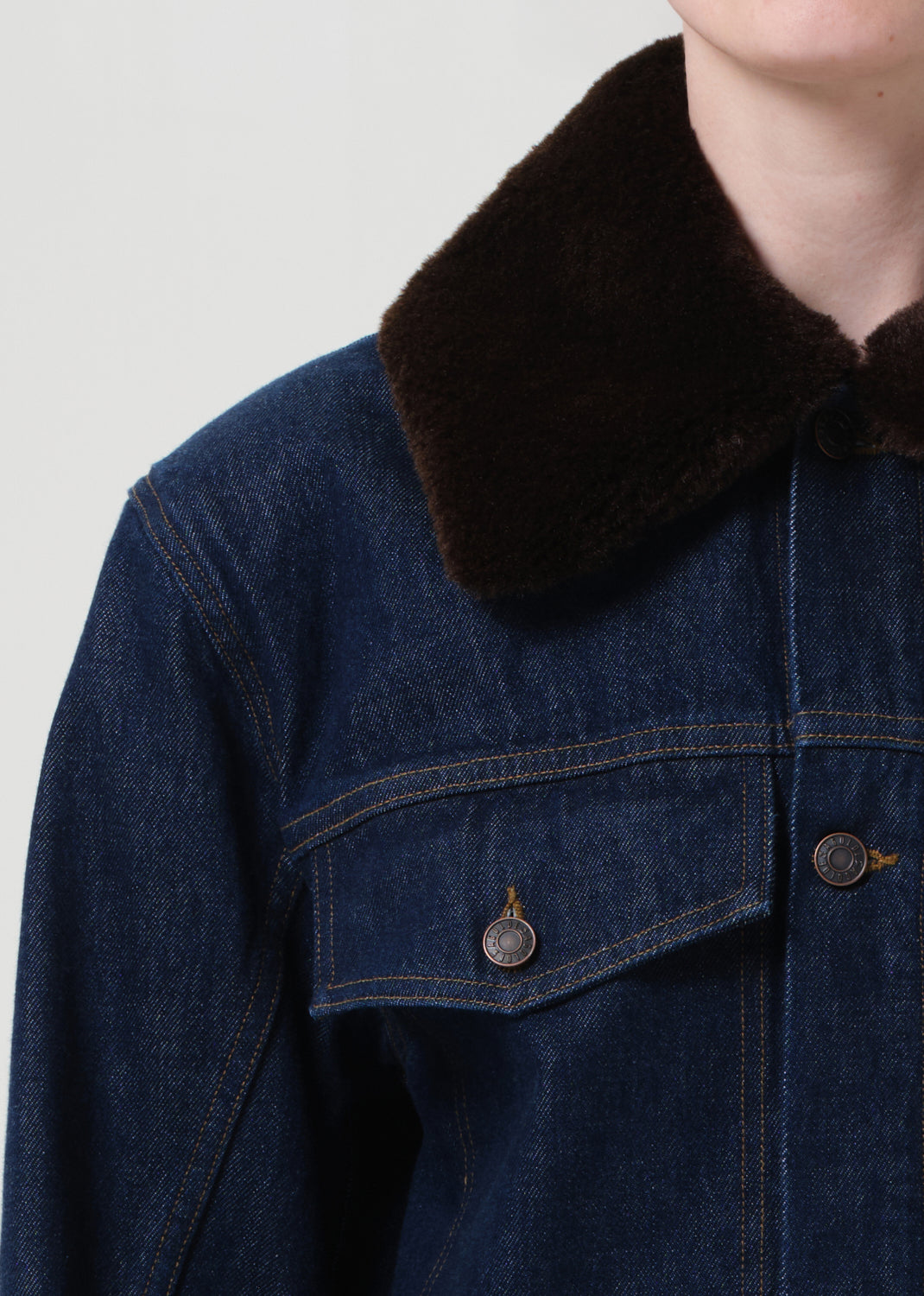 Denim jacket with a dark brown fur collar on a plain background