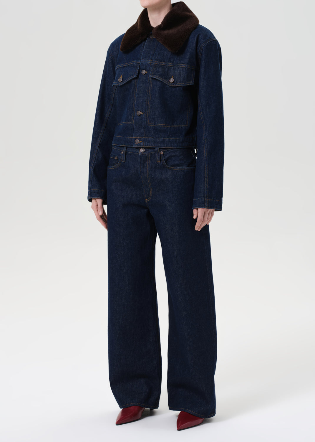 Person wearing a dark denim jumpsuit with a brown collar on a white background
