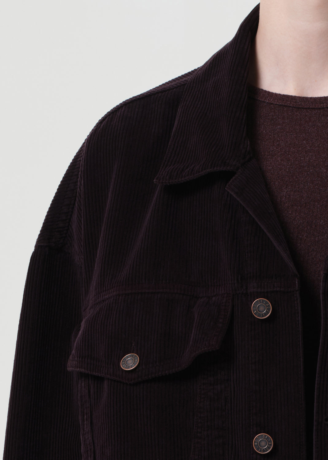 Close-up of a dark brown corduroy jacket with button details on a light gray background