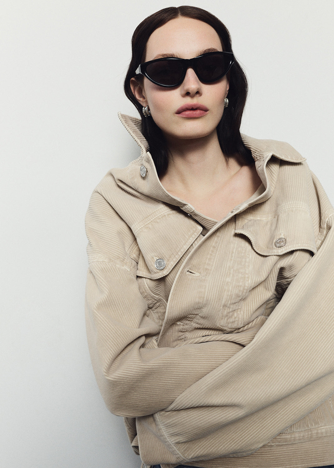 Person wearing a beige jacket and sunglasses against a white background