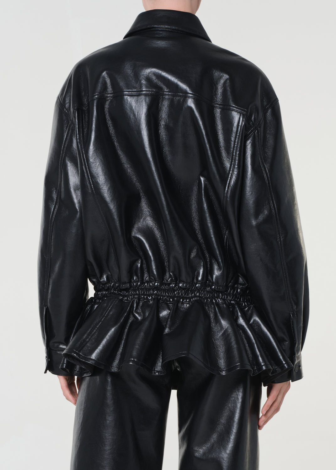 Person wearing a black shiny jacket and pants on a white background