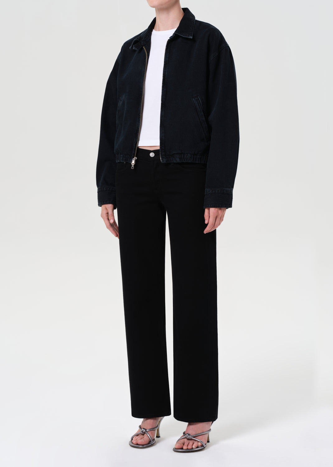 Person wearing a blue denim jacket over a white shirt and black pants on a light gray background