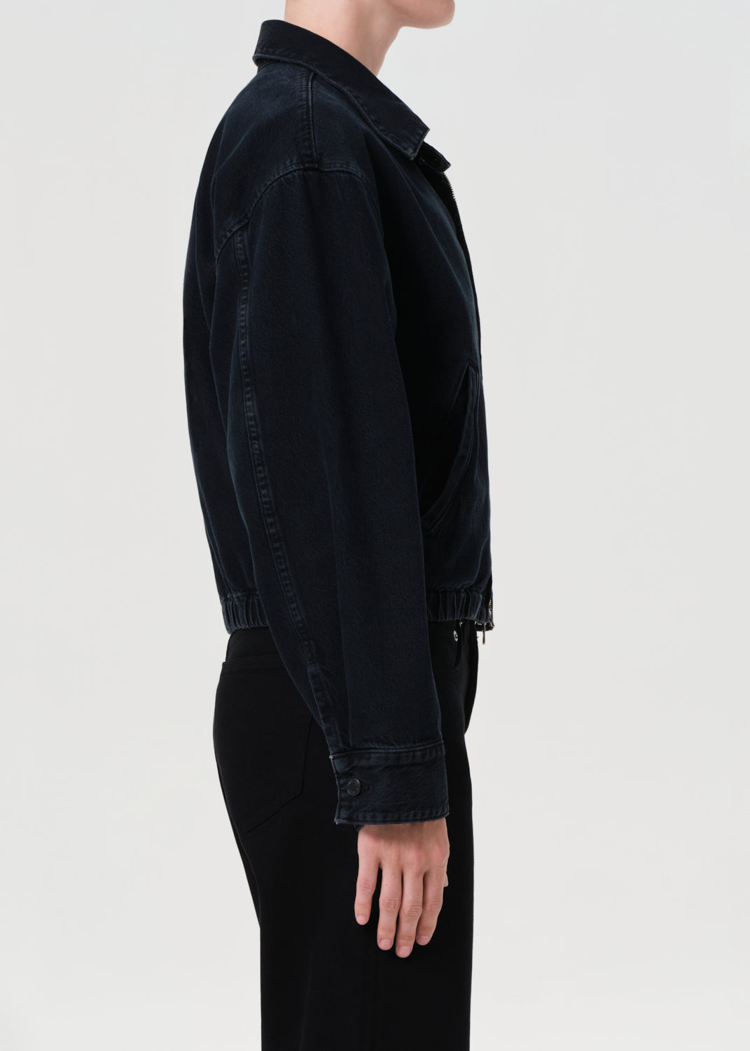 Person wearing a blue denim jacket over a white shirt and black pants on a light gray background