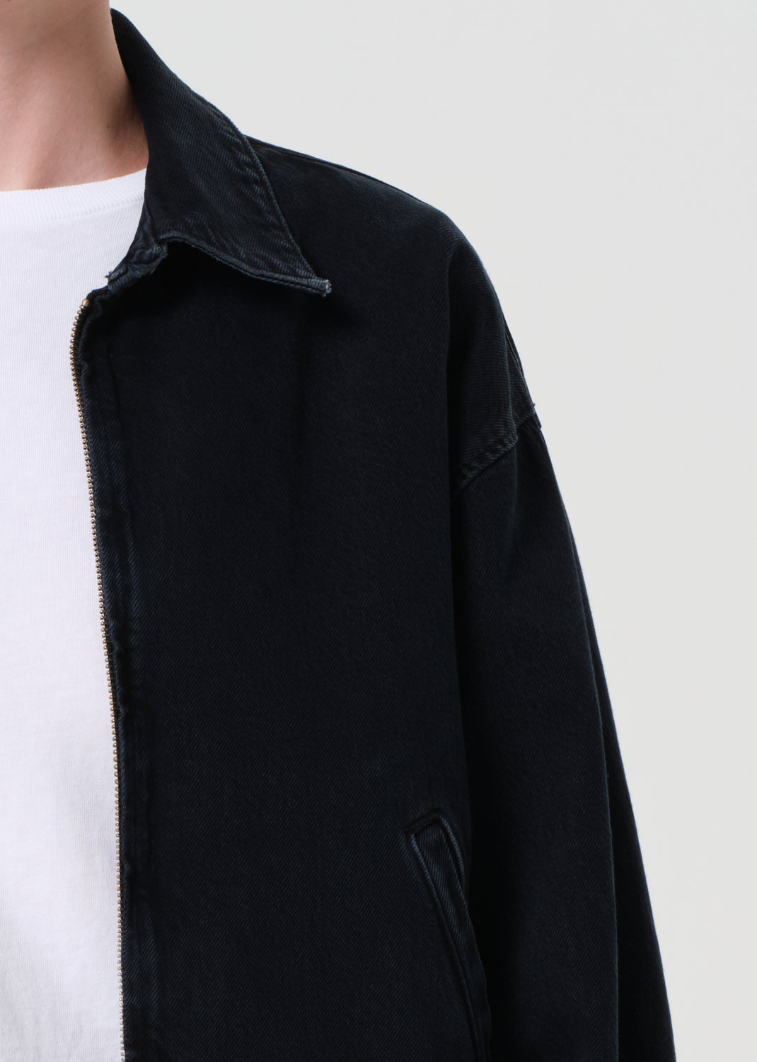 Person wearing a blue denim jacket over a white shirt and black pants on a light gray background