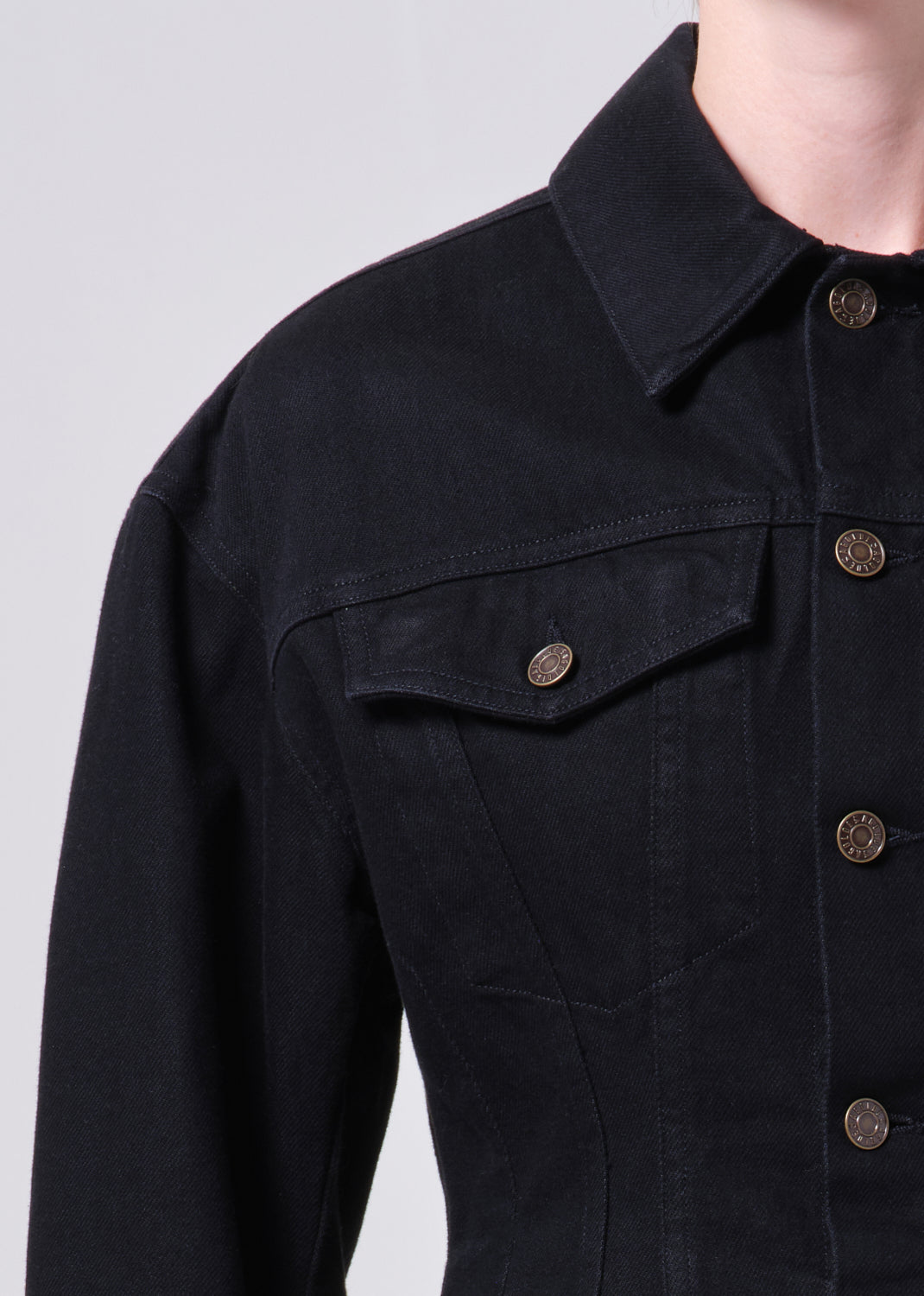 Close-up of a black denim jacket with button details on a light gray background
