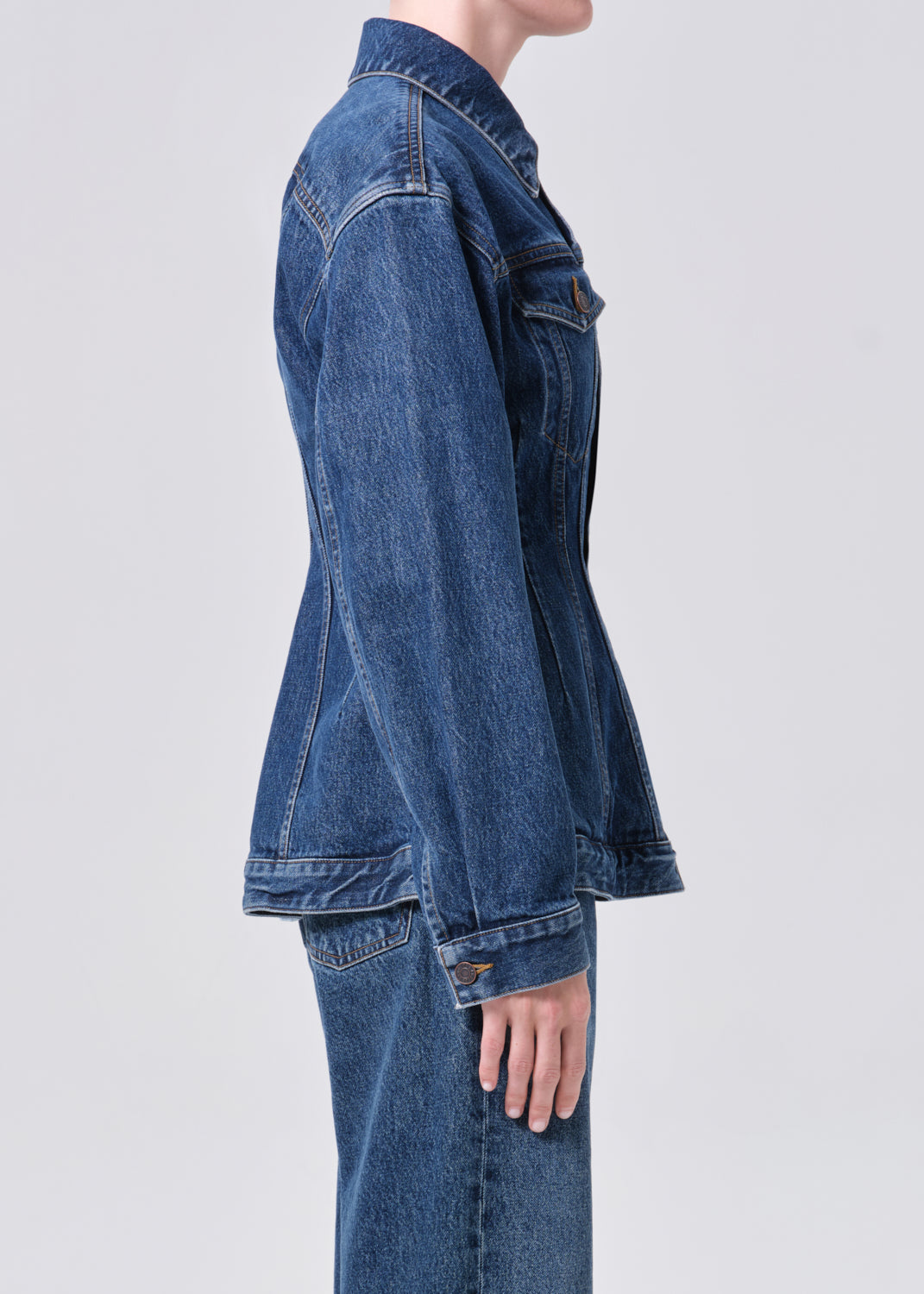 Person wearing a blue denim jacket and jeans on a light gray background