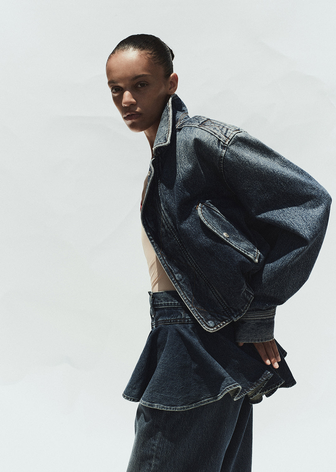Person wearing a dark denim jacket and pants on a white background