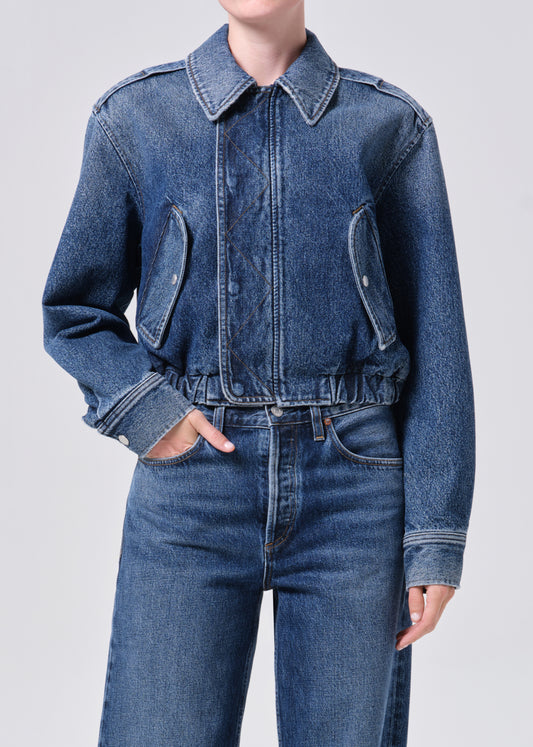 Person wearing a blue denim jacket and jeans on a light gray background