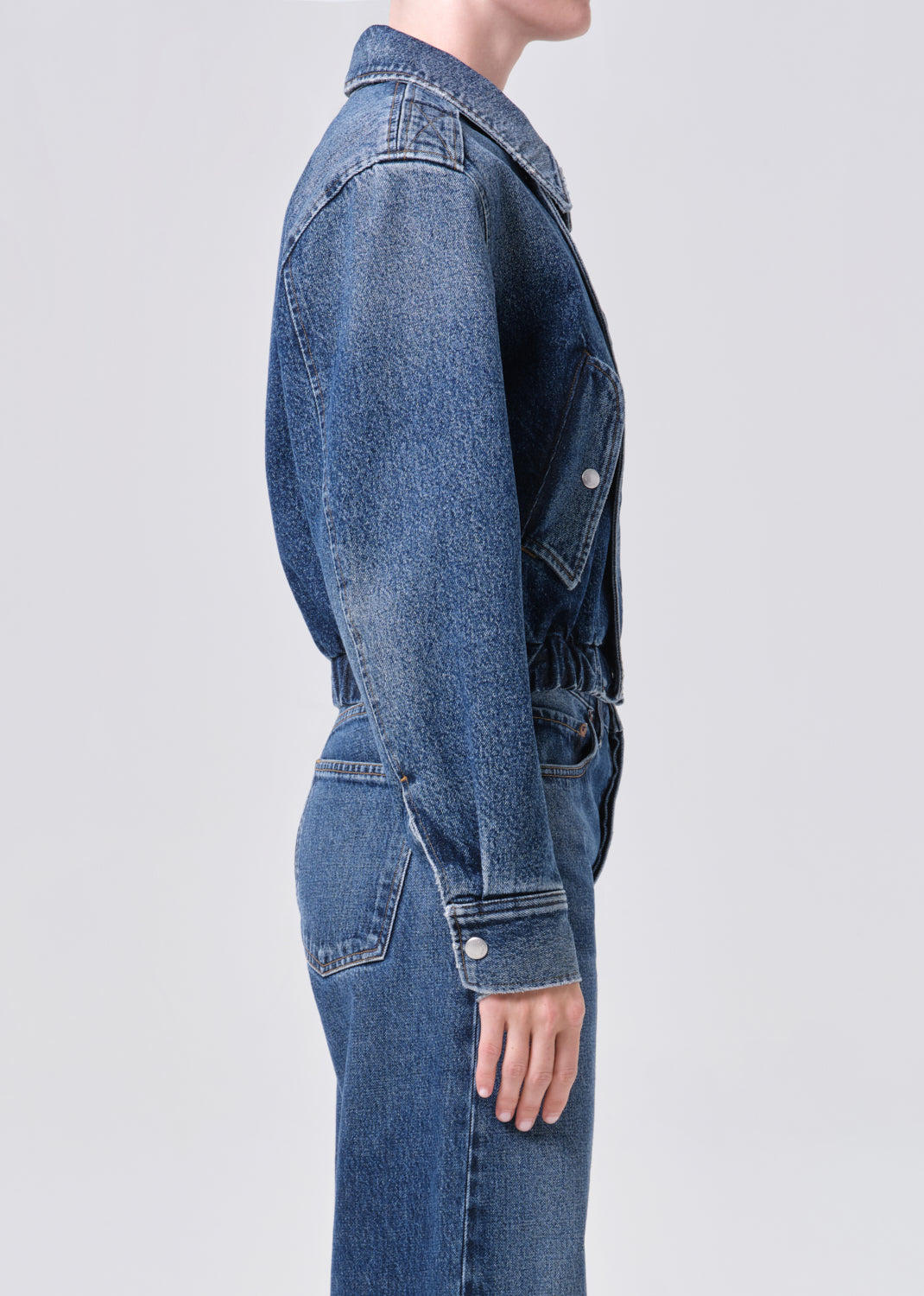 Person wearing a blue denim jacket and jeans on a light gray background