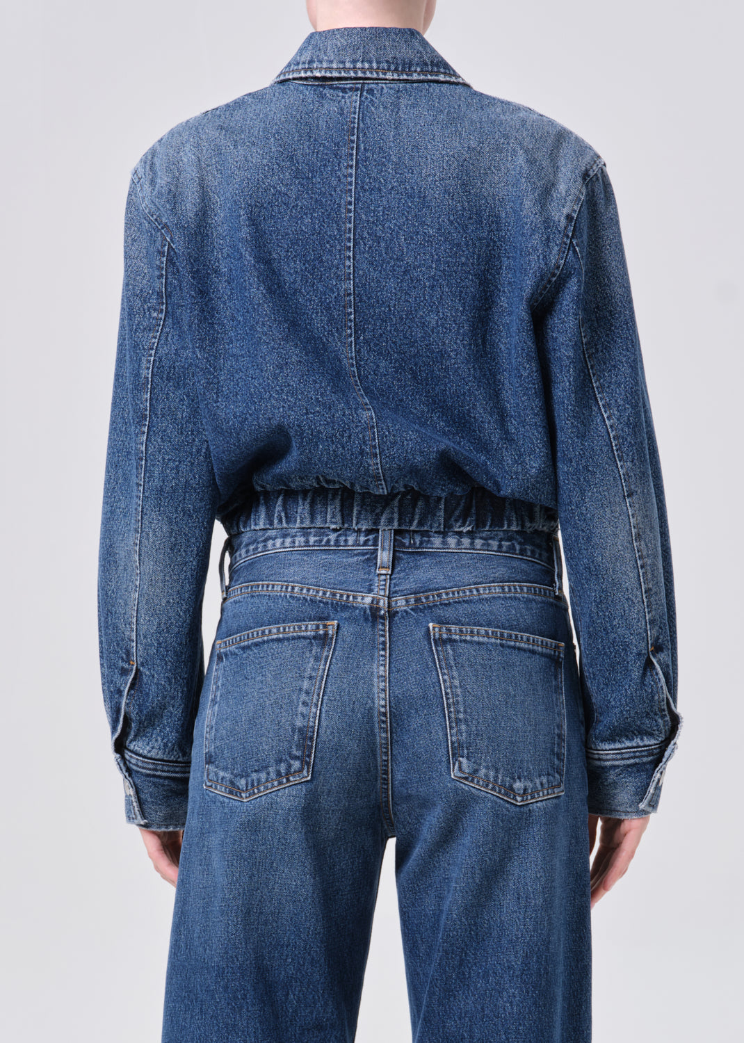 Person wearing a blue denim jumpsuit on a plain background