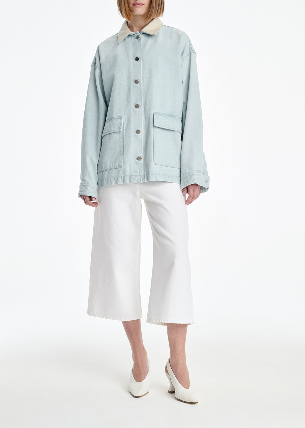 Person wearing a light blue denim jacket with a cream collar and white pants on a white background